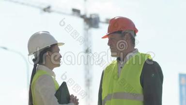 一名男子和一名年轻女子在一个建筑工地戴着头盔和信号背心。 女人向她<strong>汇报</strong>一些事情
